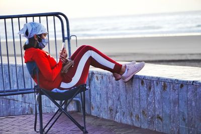 Side view of man sitting on chair at beach