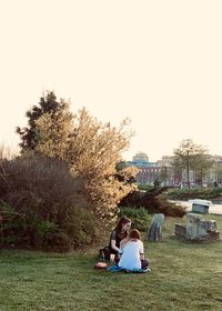 Women sitting on field against clear sky