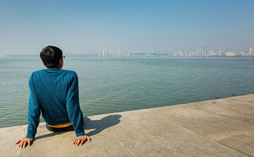 Rear view of man looking at sea against blue sky