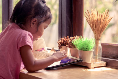 Side view of girl using digital tablet by window at home