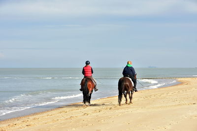 Rear view of men riding horse on beach