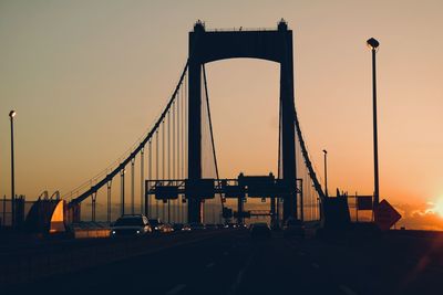 Cars moving on bridge against sky during sunset