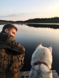 Rear view of man with dog by lake against sky