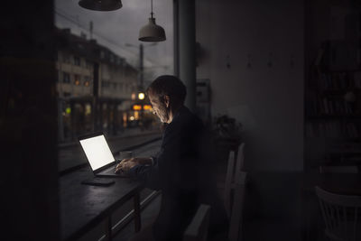 Businessman working on laptop in dark at cafe