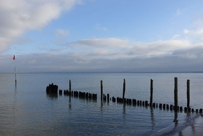 Wooden posts in sea against sky