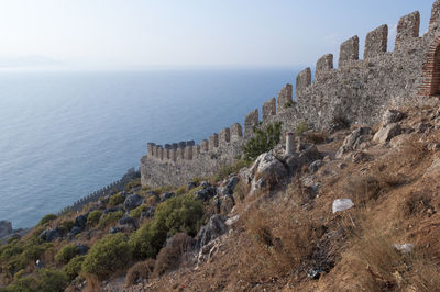 Fortified wall on mountain by sea against sky
