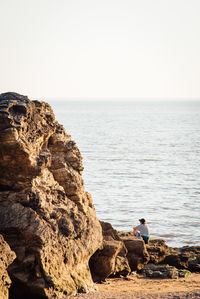 People on rocks by sea against clear sky