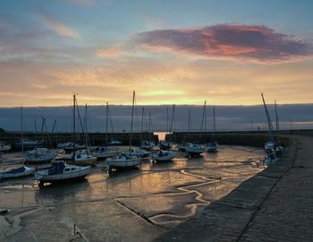 Sailboats moored at harbor during sunset