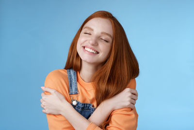 Young woman hugging self against blue background