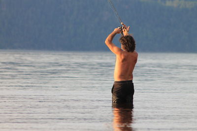 Rear view of shirtless mature man fishing in sea
