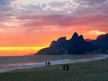 People on beach against sky during sunset