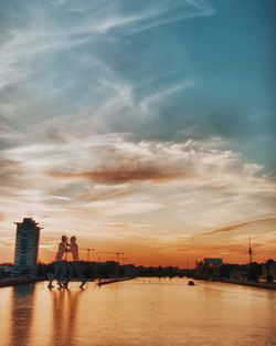 Scenic view of river by buildings against sky during sunset