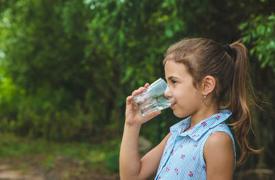 Side view of girl drinking water from glass while looking away