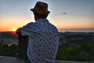 Rear view of man looking at sea against sky during sunset