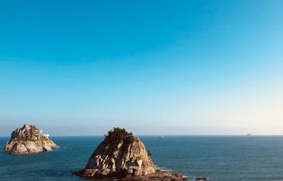 Scenic view of rock formation in sea against clear blue sky