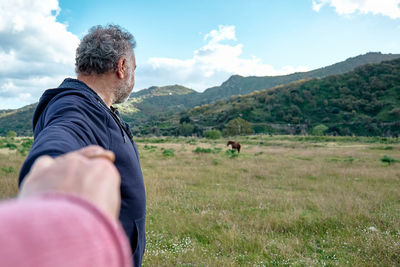 Follow me. man holds and pulls the photographer's hand while walking on the pasture