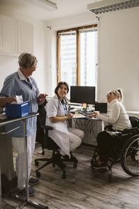 Full length of cheerful female doctor and disabled woman looking at senior nurse in medical clinic