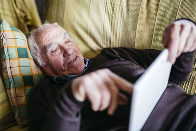 Senior man lying on couch using tablet