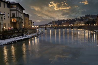 River by illuminated buildings against sky at sunset