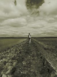 Rear view of man walking against cloudy sky