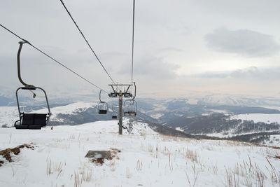 Ski lift on snow covered field against cloudy sky