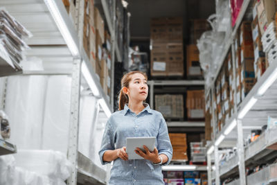 Side view of woman holding digital tablet while standing in warehouse