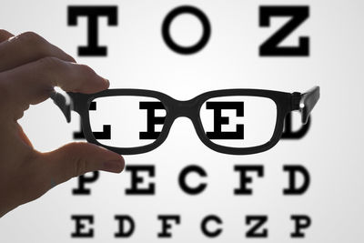 Cropped hand of person holding eyeglasses against text