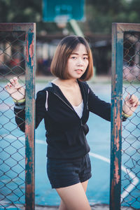 Portrait of woman standing against fence