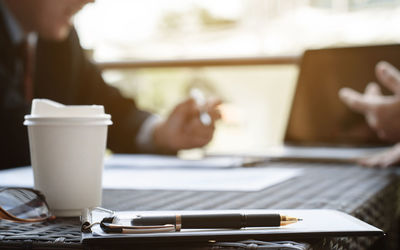 Business colleagues working with disposable cup in foreground