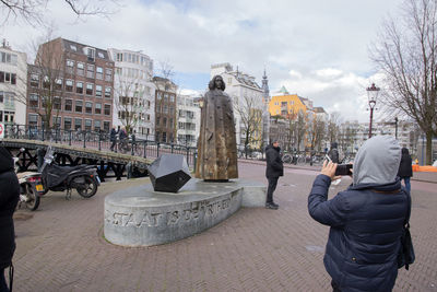 People photographing sculpture in city against sky