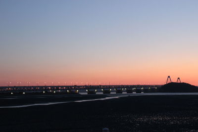 Silhouette bridge over river against clear sky at sunset