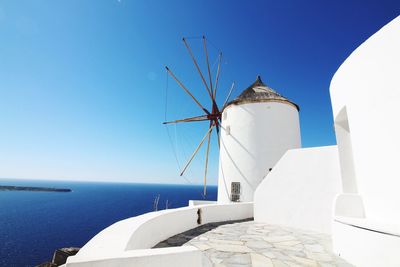 Traditional windmill by sea against clear blue sky