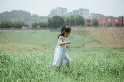 Side view of girl walking on grass in field