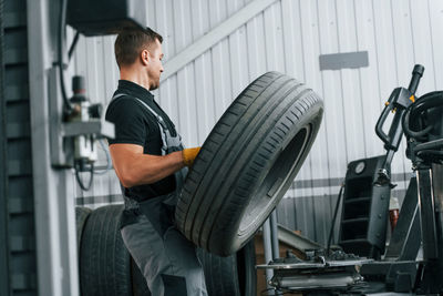 Walking and holding tyre. man in uniform is working in the auto service.