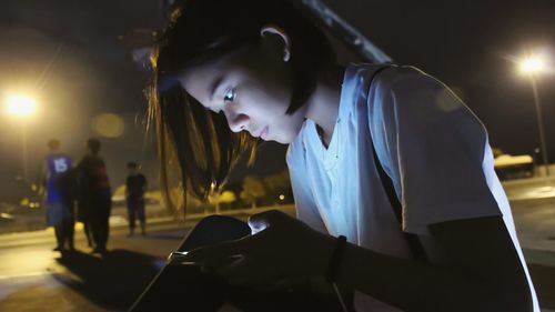 Woman using smart phone against illuminated city street at night