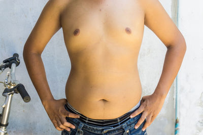 Midsection of shirtless man standing against wall