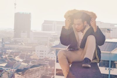 Full length of man sitting on retaining wall at building terrace