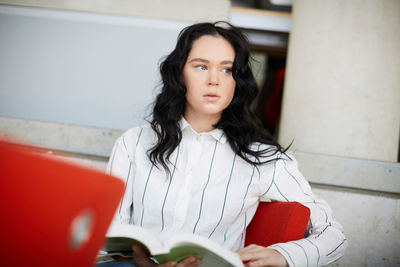 Thoughtful woman with book sitting at cafeteria in university