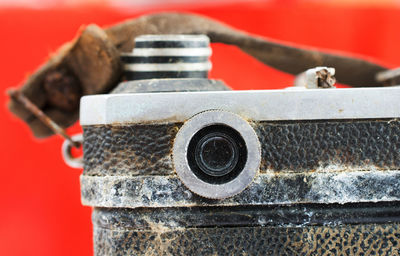 Close-up of damaged vintage camera against red background