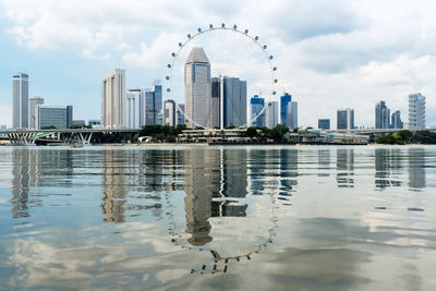 Singapore flyer by bay of water against sky in city
