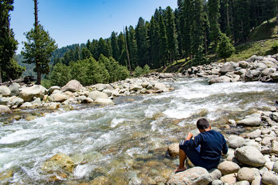 Rear view of boy sitting on rock