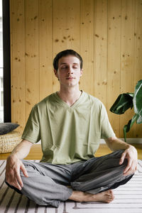 Young man meditating while sitting cross-legged at home