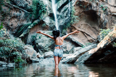 Rear view of woman standing on rock at waterfall