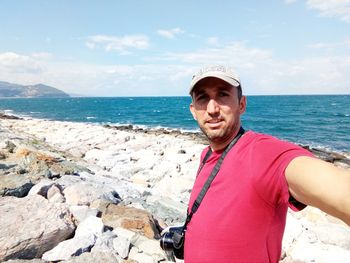 Portrait of mature man on rock at beach against sky