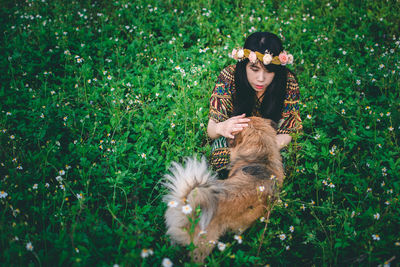 Woman wearing flowers while sitting with dog on field 