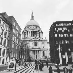 People walking in front of building against sky in city