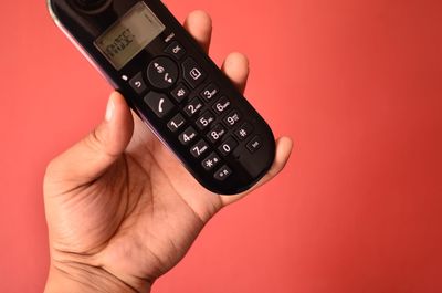 Close-up of cropped hand holding mobile phone against red background