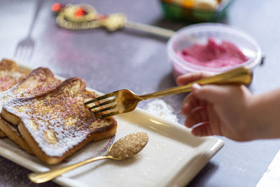 A kid hand sticks a fork in the traditional french toast with cinnamon on a gray background