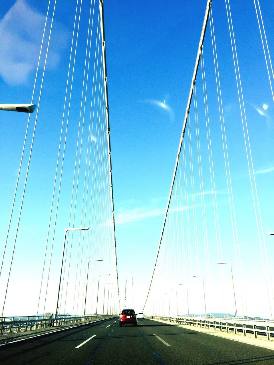 transportation, bridge - man made structure, connection, suspension bridge, engineering, car, road, the way forward, bridge, architecture, land vehicle, mode of transport, sky, built structure, highway, outdoors, travel, cable, day, blue, travel destinations, no people, low angle view, city, line