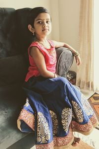 Portrait of cute girl wearing traditional clothing while sitting on sofa at home